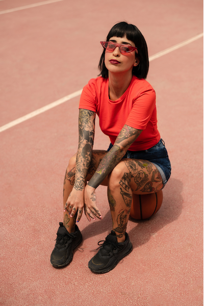 Colombian woman with a lot of tattoos sitting on a basketball.