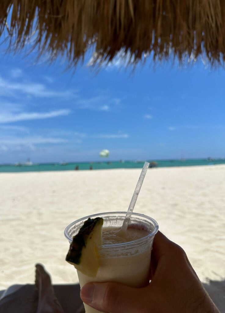 Image overlooking the Bavaro beach in Punta Cana while sipping a non-alcoholic Pina Colada, sitting under a cabana.