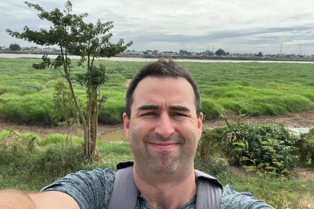 American man standing on Mekong riverbank on Vientiane, Laos side. Other side of river is Nong Khai, Thailand.